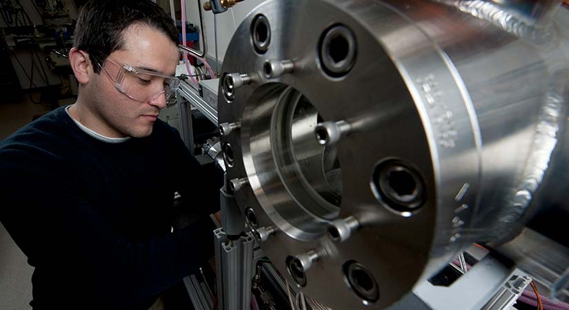 Man operating laboratory equipment, specifically a boiling vessel with cooling loops.