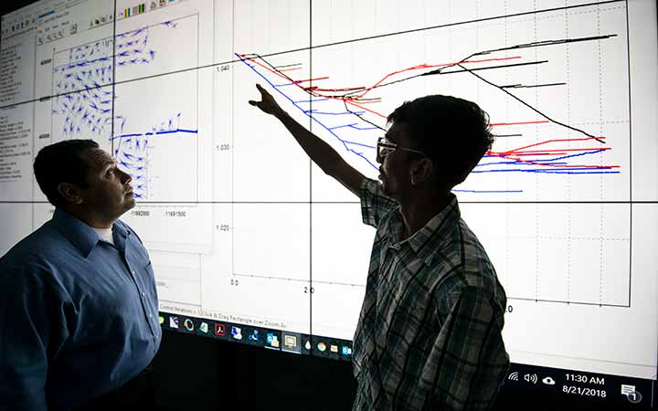 Two researchers review a large projection of a multi-timescale simulation environment.